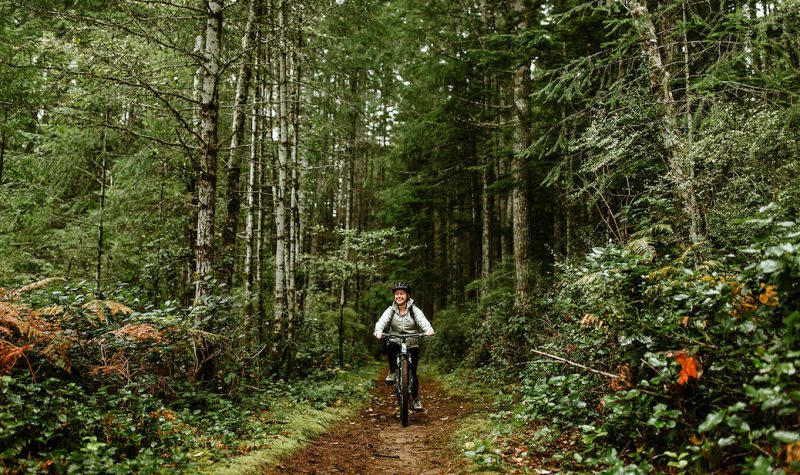 A woman cycling along a trail through the woods on Cortes Island