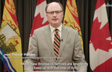 A man standing in front of a number of Canada and New Brunswick flags