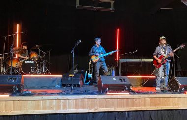 3 jeunes élèves sont sur la scène et jouent de la guitare.