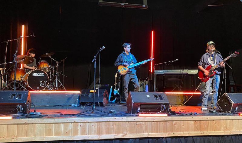 3 jeunes élèves sont sur la scène et jouent de la guitare.
