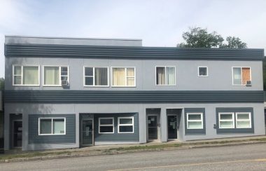 Two story building painted two shades of grey with multiple windows and doors.