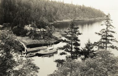 A black and white photo reveals an old boat on a private dock, on a secluded island.