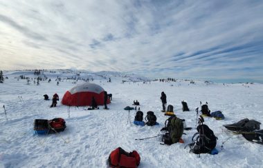 Des personnes dehors dans la neige sur un camp de base avec des tentes et des sac à dos