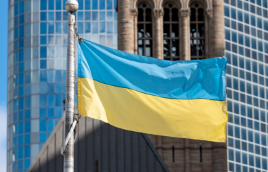 A blue and yellow flag hanging on a metal pole in front of a large glass building.