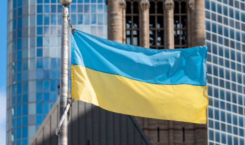 A blue and yellow flag hanging on a metal pole in front of a large glass building.