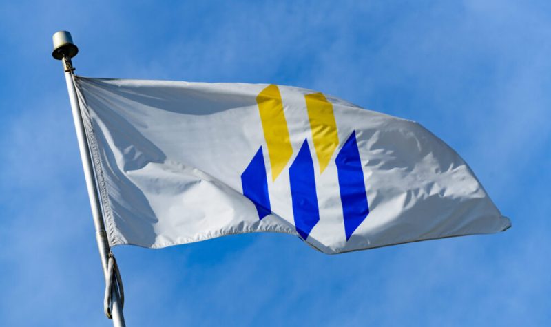 Un drapeau de l'université de Moncton qui vole au vent devant un ciel bleu