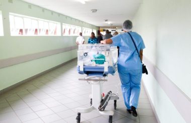 A healthcare worker transports a patient down a hallway wearing scrubs.