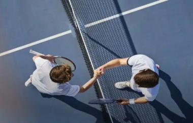 Two tennis players in white outfits shake hands over top of the net at centre court.