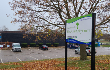 A leaf-covered lawn sits before the Jefferson Elora Community Centre parking lot. The sign notes the name of the building.