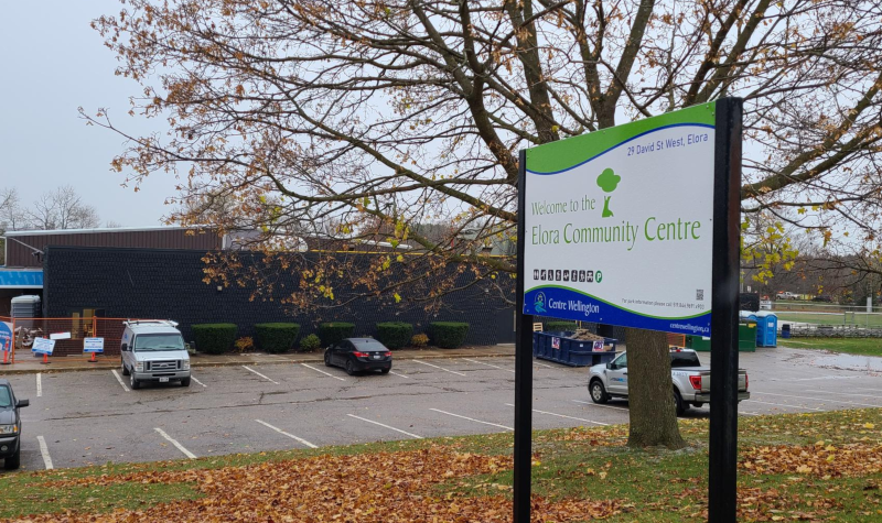 A leaf-covered lawn sits before the Jefferson Elora Community Centre parking lot. The sign notes the name of the building.