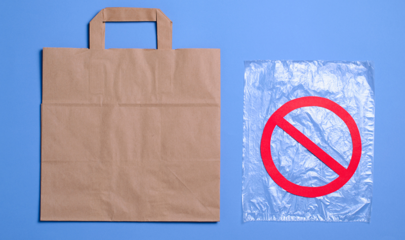 A plastic bag with a 'no' sign through it next to a brown paper bag on a blue background.