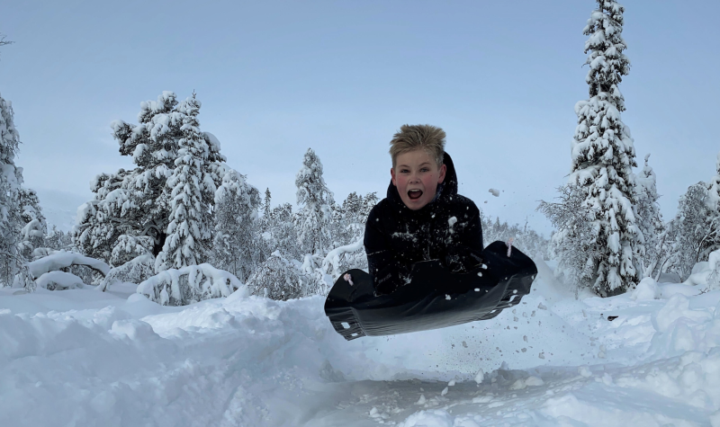 A child flies through the air on a toboggan amid the snowy conditions on a hill.