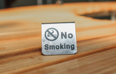 A metal no smoking sign sits on a wooden countertop in a well-lit room.