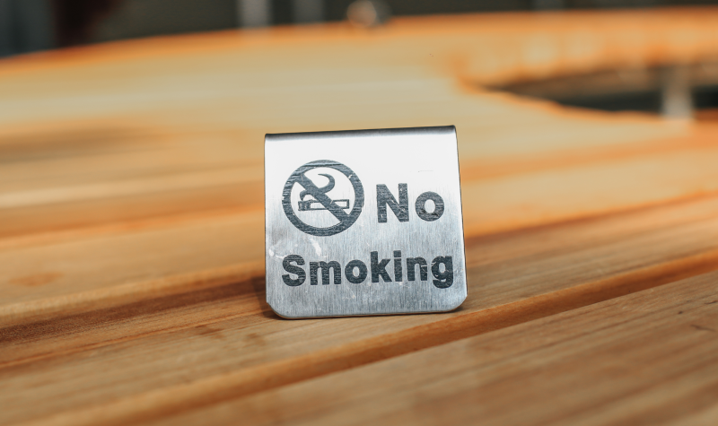 A metal no smoking sign sits on a wooden countertop in a well-lit room.