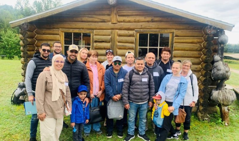 Une quinzaine de personnes à l'extérieur devant un petit chalet en bois à la lumière du jour