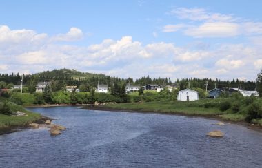 Quelques maisons entrecoupées de forêt aux abords d'une rivière, à l'avant-plan.