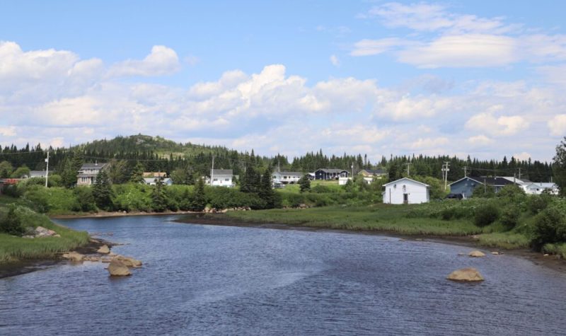 Quelques maisons entrecoupées de forêt aux abords d'une rivière, à l'avant-plan.