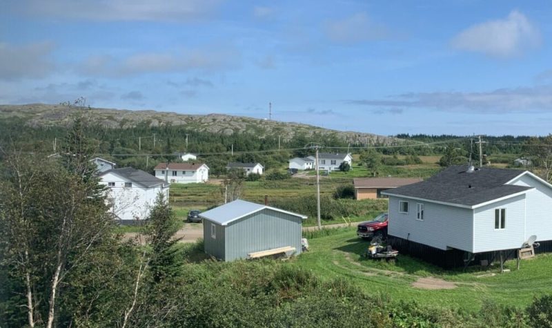 Des maisons rapprochés au coeur d'un village vert de verdure, d'arbres et de mornes.