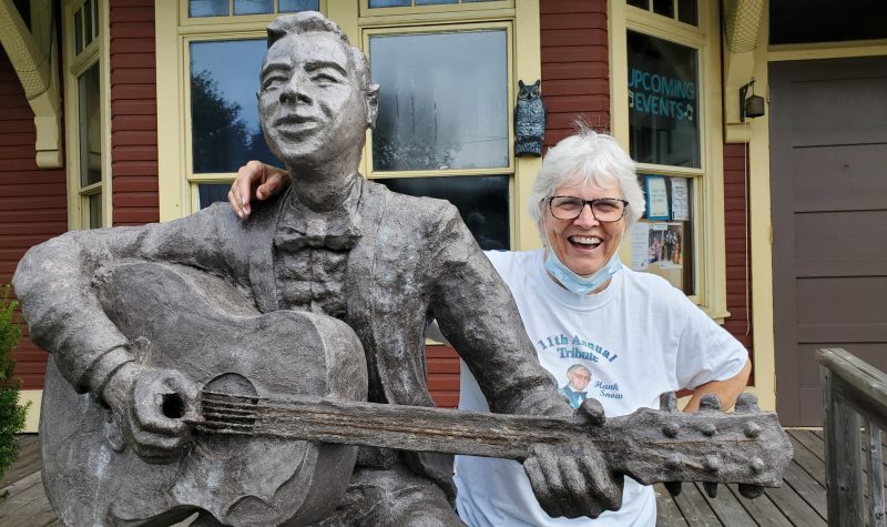 A smiling woman has her arm around a statue of a man playing guitar