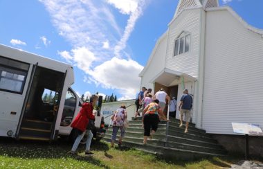 Des gens sortent d'un minibus pour entrer dans une église sous un ciel bleu et ensoleillé.