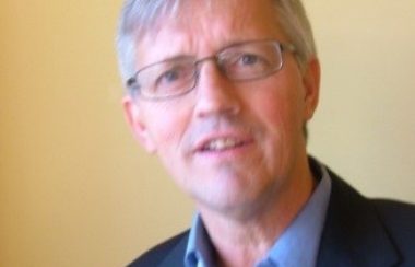 A headshot of John Vissers with a beige wall behind him