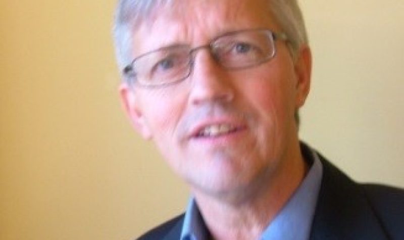 A headshot of John Vissers with a beige wall behind him