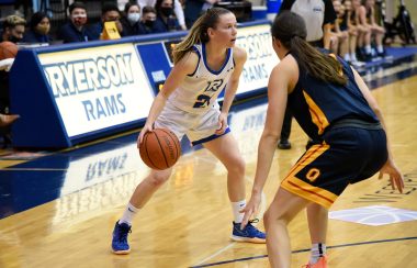 A woman in a white and blue basketball uniform dribbles a ball on a court during a game.