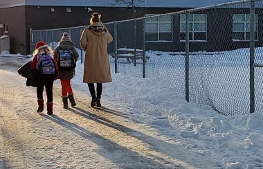 A parent walks to small children to school along a snowy path