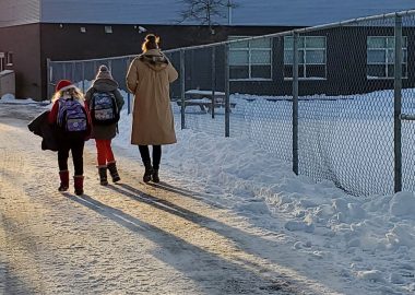 A parent walks to small children to school along a snowy path