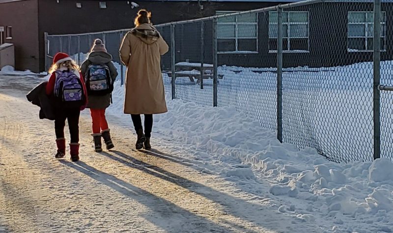 A parent walks to small children to school along a snowy path