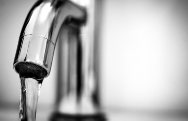 A grey faucet drips water in front of a blurred background.