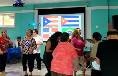 Personas bailando frente a las banderas de República Dominicana, Puerto Rico, Cuba y Brasil.