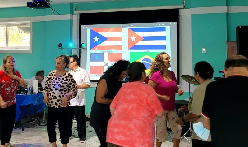 Personas bailando frente a las banderas de República Dominicana, Puerto Rico, Cuba y Brasil.
