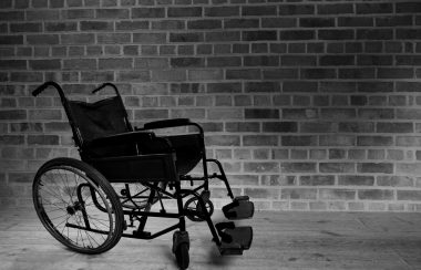 A black and white photo of a wheelchair next to a brick wall.