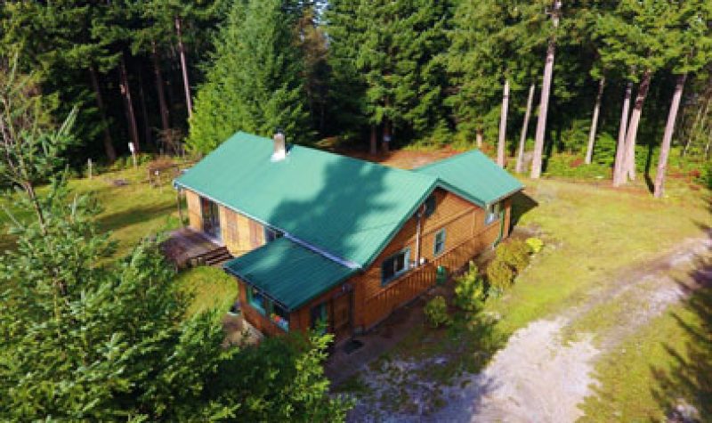 An aerial shot of house with tin green roof, wood siding, trees & grass around