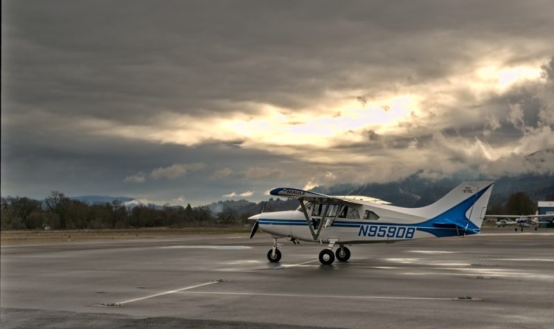 Un petit avion blanc et bleu sur une piste d'atterrissage sous un ciel gris avec un éclaircis.