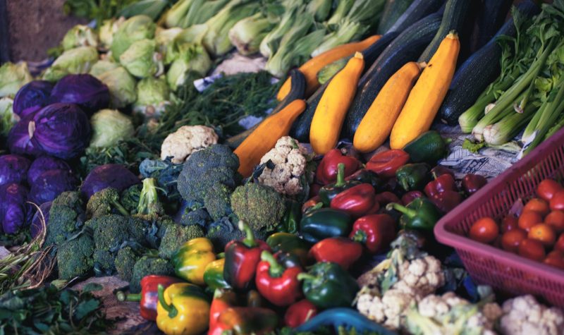Des légumes dans un présentoir. Parmi ceux-ci on retrouve brocolis, poivrons, tomates, choux-fleurs et courgettes