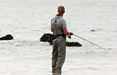 Un homme debout sur le bord de l'eau avec une canne à pêche en main