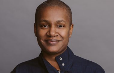 A woman standing in front of a grey background.