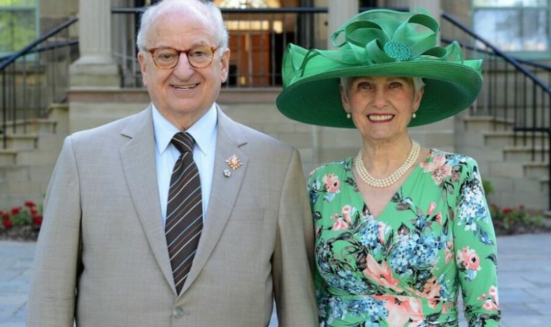 Un homme portant un gilet brun et une femme portant une robe et un chapeau vert.