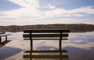 A bench is surrounded by water from a spring flood in Quebec on a sunny day