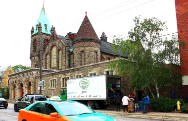 A large church made of brown bricks with a white truck and taxi in front of it on the streets.