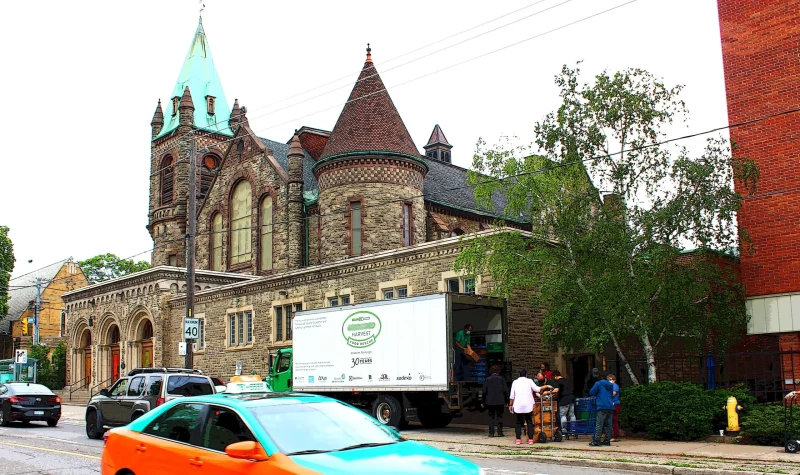 A large church made of brown bricks with a white truck and taxi in front of it on the streets.
