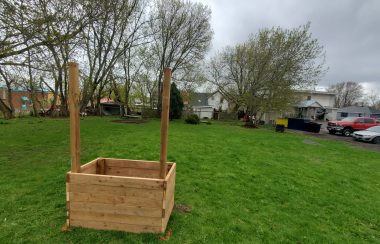 A partially constructed sign and garden box on an empty lot of grass.