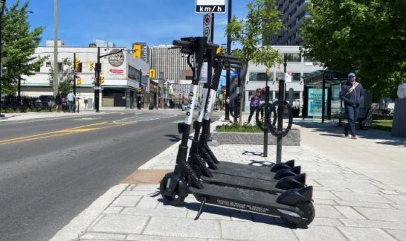 Three electronic scooters are lined up on a curb beside a street in downtown Ottawa.
