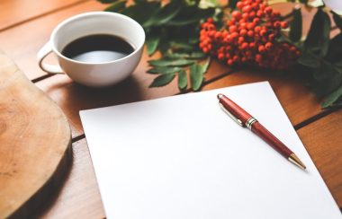 Crayon posé sur une feuille blanche , ceci sur une table en bois ou est déposé à coté une tasse de café et un rameau de plante.