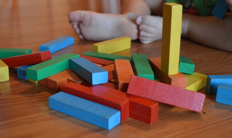 A toddler's feet on a wooden floor with multicoloured building blocks.