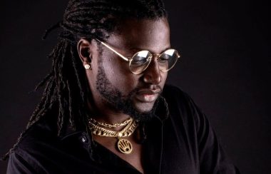 Bo diaw sur fond noir, portant des lunettes rondes et plusieurs bijoux dorés