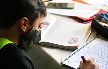 Jeune garçon qui écrit dans un cahier avec un masque