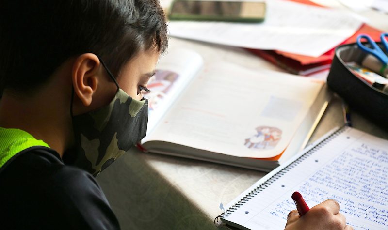 Jeune garçon qui écrit dans un cahier avec un masque